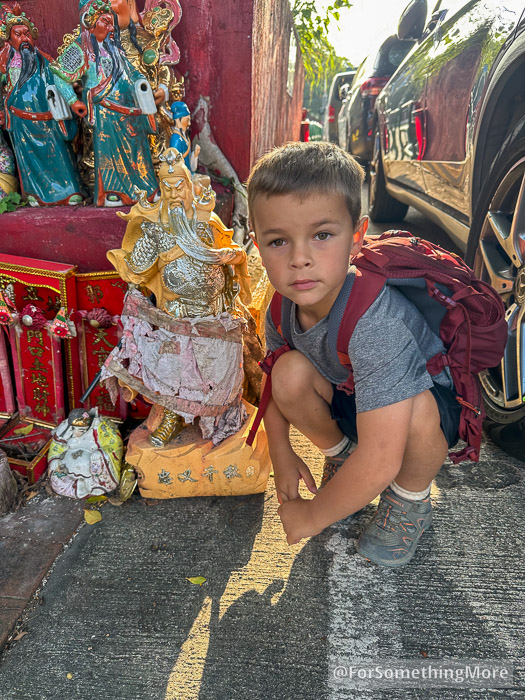 Boy crouching near Taoist God statues on his Tai To Yan hike
